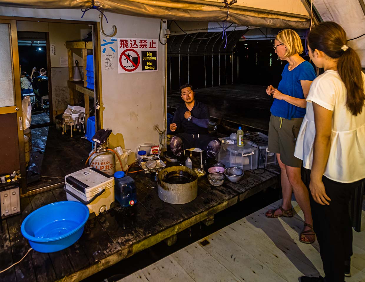 Fischer, Koch und Entertainer. Mit simpelstem Equipment begibt sich Ikuya Yamamoto an die Zubereitung des Fangs. Geschickt werden die Fische geputzt und die Krebse kommen in den Kochtopf. Gäste stellen neugierig Fragen und werden mit einem kühlen Getränk versorgt / © Foto: Georg Berg