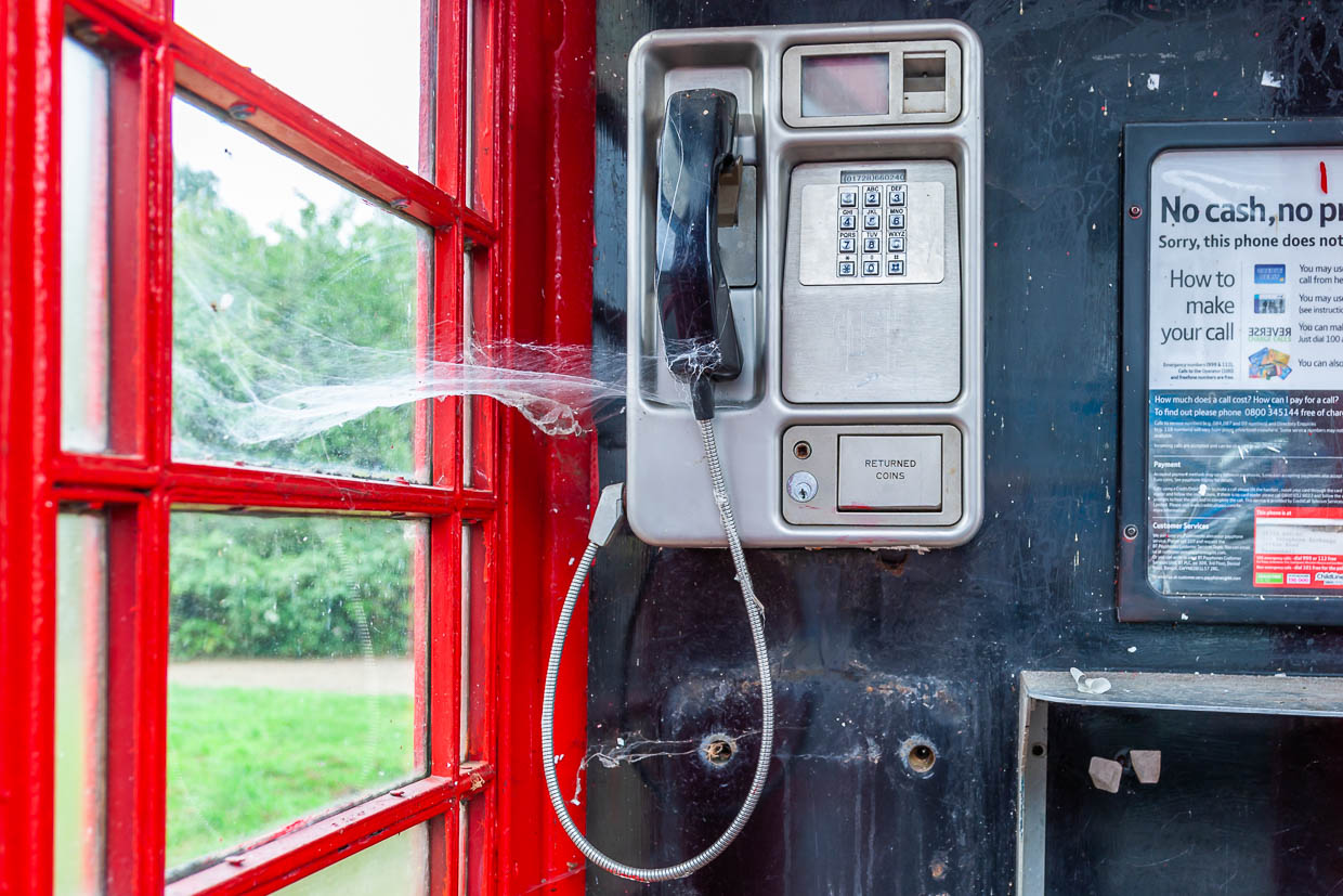 Une cabine téléphonique rouge traditionnelle dans un environnement rural au Royaume-Uni montre une toile d'araignée au-dessus du combiné / © Photo : Georg Berg