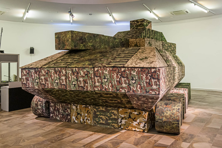 La guerre - un thème récurrent à la documenta. Des modules de sièges en camouflage de taches sont assemblés deux fois par semaine lors d'une performance pour former un char d'assaut grandeur nature / © Photo : Georg Berg
