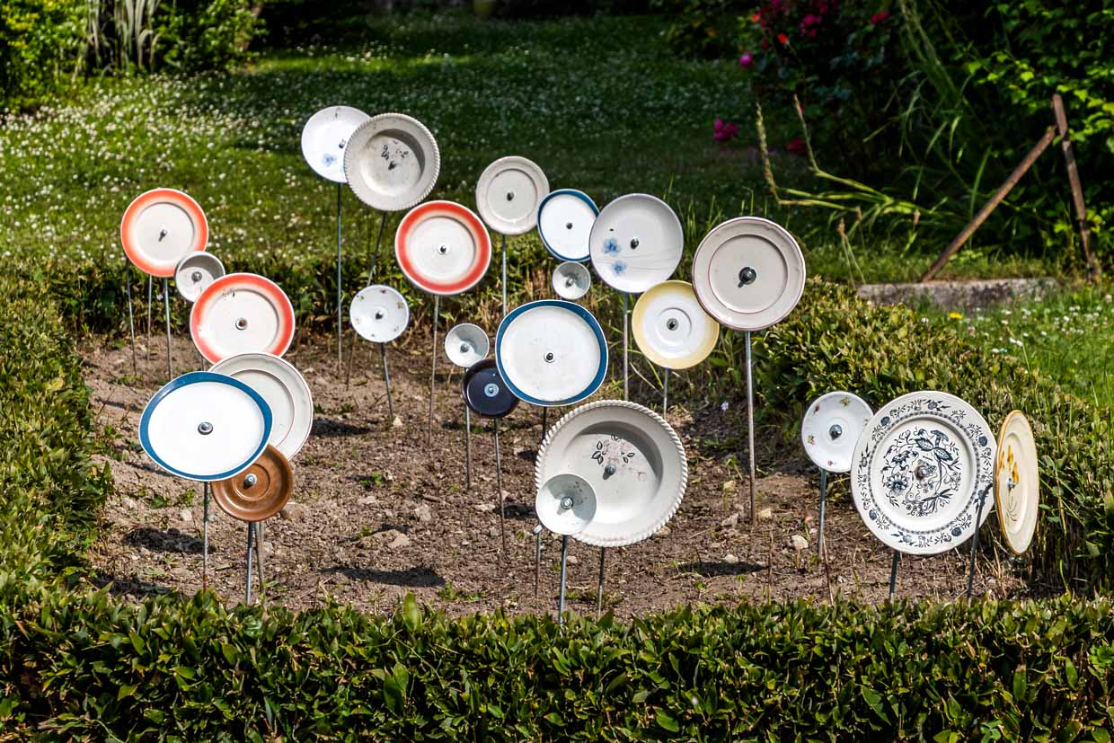 Assiettes sur des barres dans un jardin de devant en France, Nouvelle-Aqutaine. Le motif correspond au proverbe allemand "Über den Tellerrand schauen" et signifie une attitude ouverte et curieuse, où l'on est prêt à dépasser ses propres limites et à découvrir de nouvelles choses. L'expression est souvent utilisée en relation avec l'ouverture au monde, le changement de perspective ou l'innovation / © Photo : Georg Berg