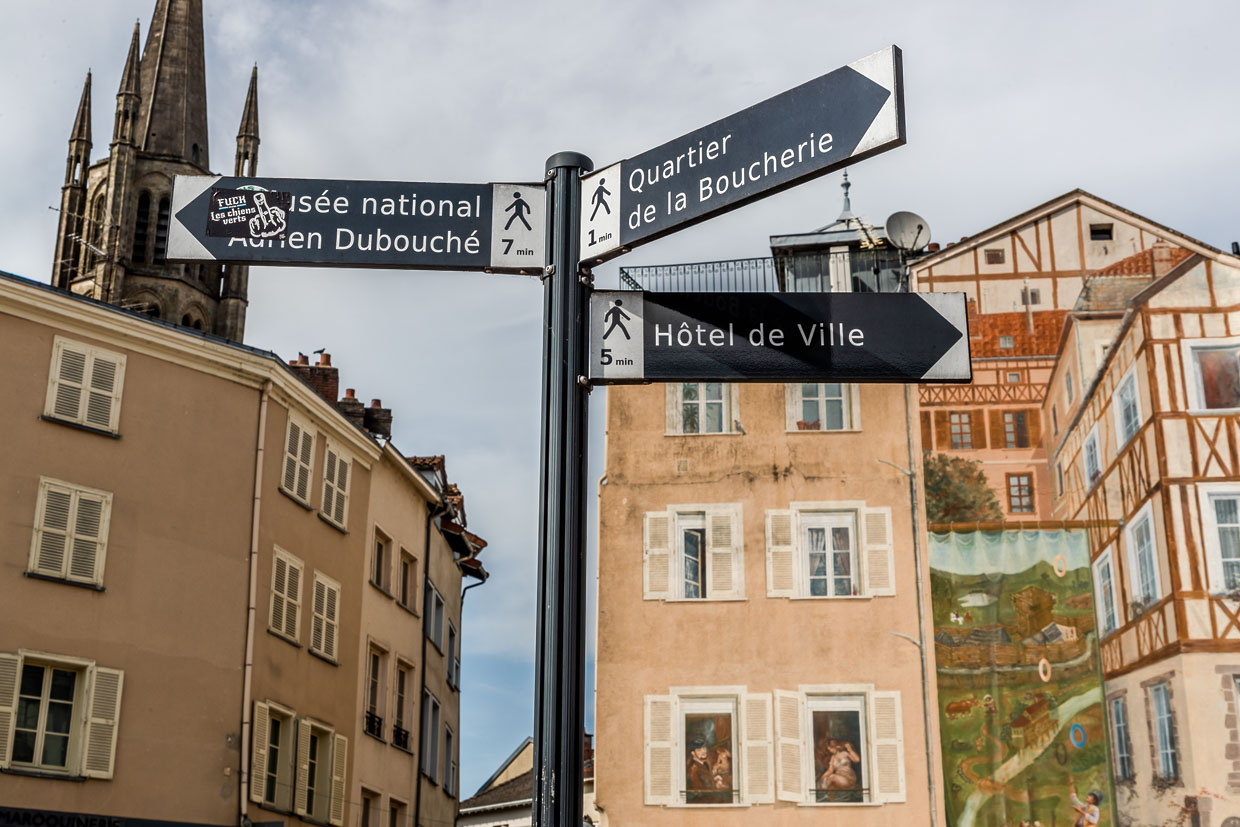 Panneaux indicateurs dans le centre de Limoges, indiquant les lieux à visiter dans la ville, comme le Musée National Adrien Dubouché, le quartier des bouchers et l'hôtel de ville, avec en arrière-plan une peinture murale, dans le style des anciennes maisons à colombages / © Foto : Georg Berg
