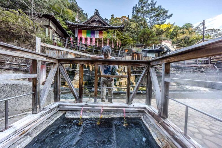 Mann betrachtet heiße Quelle mit traditionellen japanischen Bauten in Tanabe, Japan