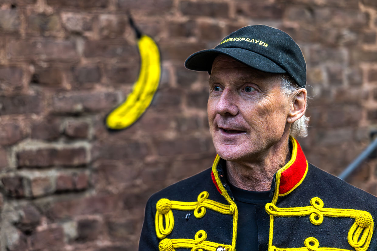 Ein Mann in Uniformjacke und Kappe steht vor einem Bananen-Graffiti am Stadtpark, Grevenbroich, Deutschland